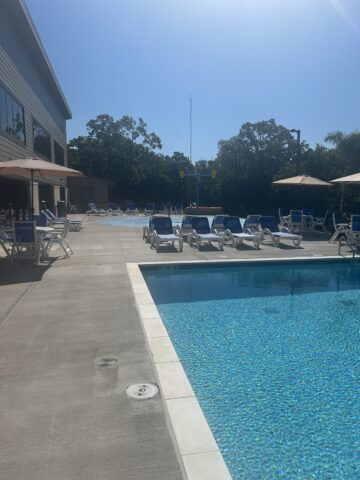 image of aquatic center outdoor pool. including chairs, umbrella tables. splashpad in background